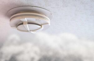 An image of a smoke detector with smoke rising within the room.