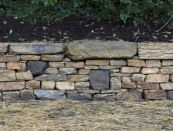 Building a dry stone retaining wall is well within your abilities. This is a great example of a retaining wall that does NOT interfere with the natural site drainage.