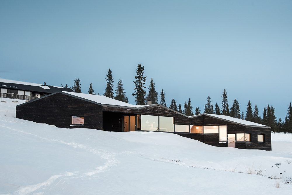 Cabin Sjusjøen's black facade stands out against the stark white backdrop.