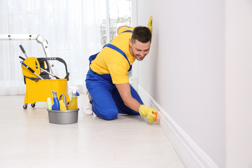 Professional janitor cleaning baseboard with brush after renovation.