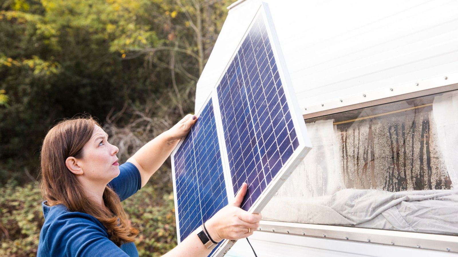 An image of a woman installing a solar panel onto her RV.